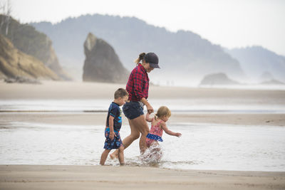 Side view of mother walking at beach with her two young kids.