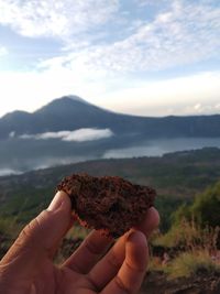 Close-up of hand holding rock against sky