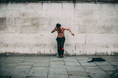 Full length rear view of shirtless man standing against wall