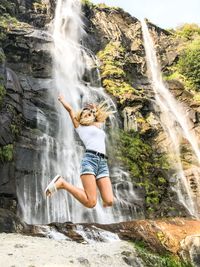 Young woman jumping against waterfall