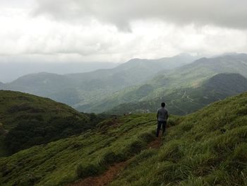 Rear view of man looking at mountains against cloudy sky