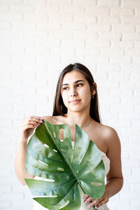 Spa and beauty. happy beautiful brunette woman wearing bath towels holding a green monstera leaf 