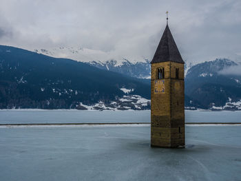 Tower in frozen lake against mountains