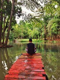 Rear view of man sitting on lake against sky