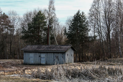 Abandoned house on field against trees in forest