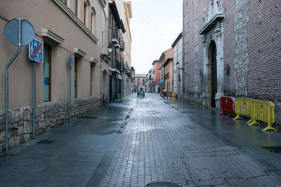 Wet street amidst city against sky