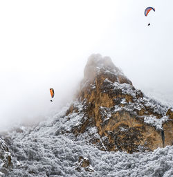 People paragliding over snow mountains against sky