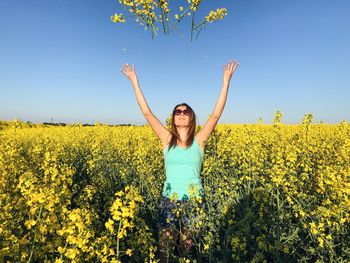 Young woman throwing yellow flowers at oilseed rape field