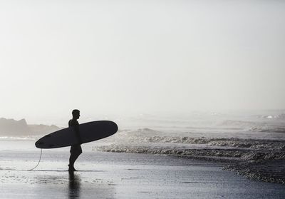 Surfer holding surfboard while standing on shore at beach