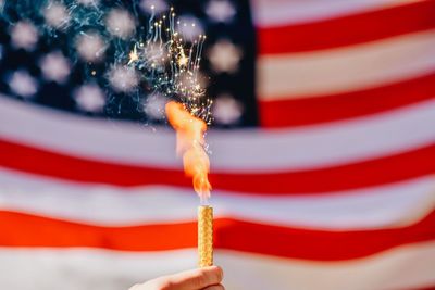 Cropped hand holding burning sparkler against american flag