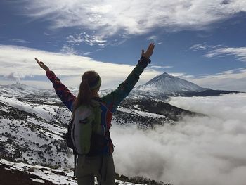 Low angle view of woman standing on snowcapped mountain against sky