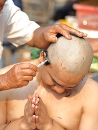 Cropped hand of man cutting hair of monk during ordination