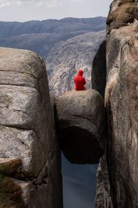 Rear view of man sitting on rock formation against sky