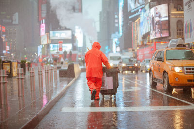 Rear view of man walking on wet street in rainy season
