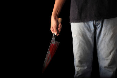 Midsection of man holding knife while standing against black background