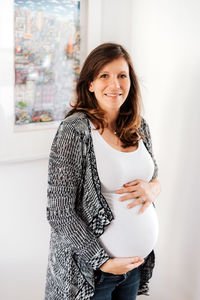 Portrait of pregnant woman standing against wall at home