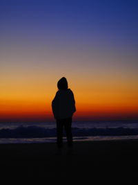 Rear view of silhouette girl standing on beach during sunrise 
