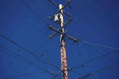 Low angle view of electricity pylon against blue sky