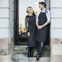 Mid adult owners looking at each other while standing on steps against doorway