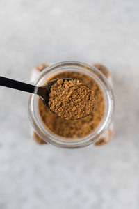 A small spoon with instant coffee granules over a glass jar of coffee.