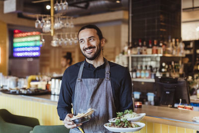 Happy male waiter with food looking away in bar