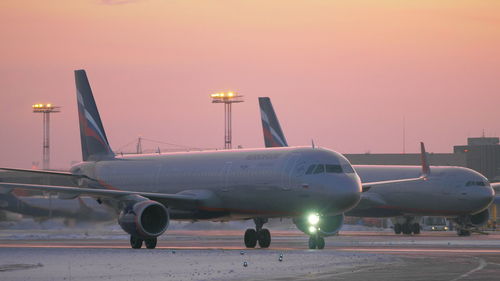 Airplane on airport runway against sky at sunset