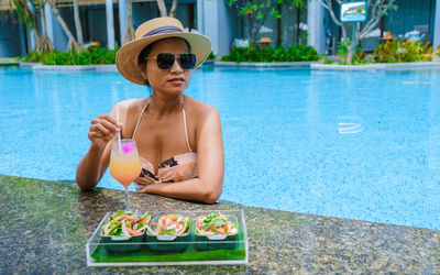 Portrait of young woman drinking water while sitting in swimming pool