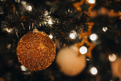 Details of christmas ball with golden glitter hanging on the christmas tree branches. winter holiday