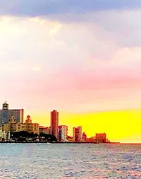 Sea by buildings against sky during sunset