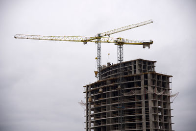 Low angle view of crane at construction site against sky