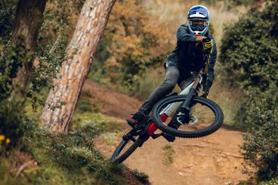 Unrecognizable man in helmet, gloves and protection glasses jumping doing whip trick downhill during mountain biking practice in wood forest