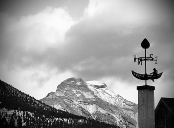 Low angle view of weather vane against cloudy sky