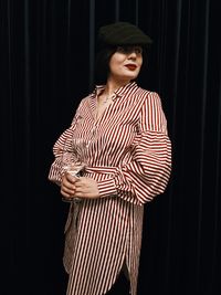 Young woman looking away while standing against black background