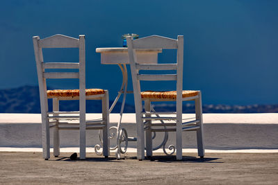 Empty chairs and table at beach against blue sky