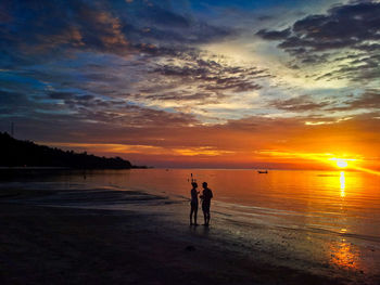 Silhouette people on beach against sky during sunset