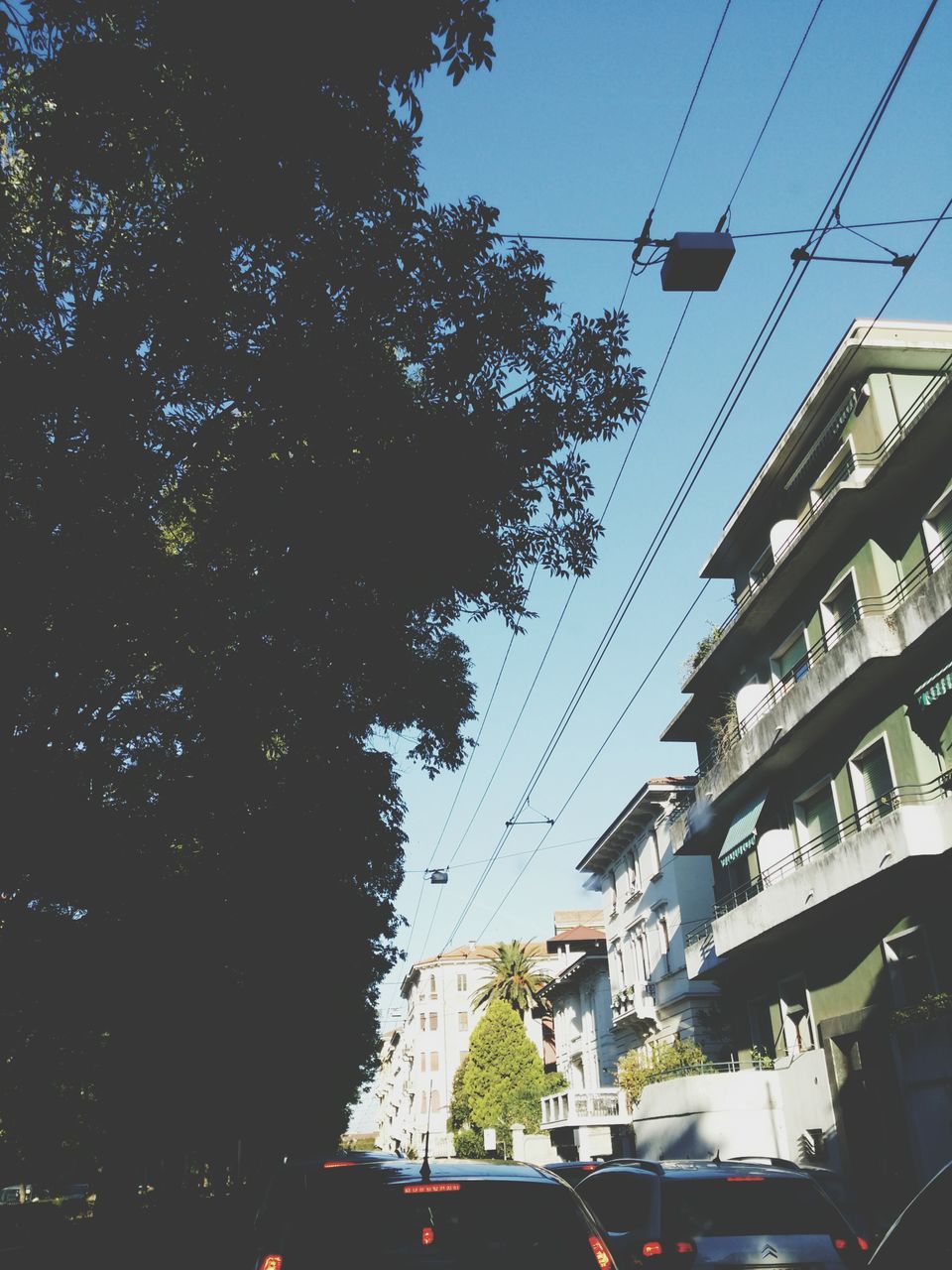 transportation, mode of transport, car, land vehicle, power line, sky, electricity pylon, street, road, cable, on the move, city, tree, traffic, built structure, electricity, low angle view, street light, travel, architecture