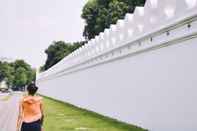 Rear view of woman standing by wall against sky