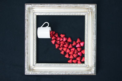 Directly above shot of red heart shapes and cup in picture frame on black background