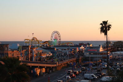 Ferris wheel by sea against clear sky at sunset