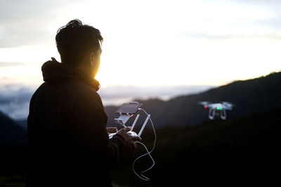 Side view of man flying drone over mountain against sky during sunset