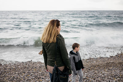 Mother and son wearing warm clothing while standing at beach