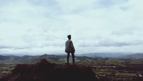 Rear view of man standing on mountain against sky