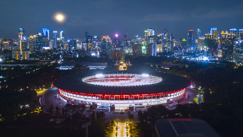 Illuminated stadium in city against sky at night