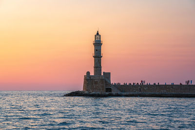 Lighthouse by sea against sky during sunset