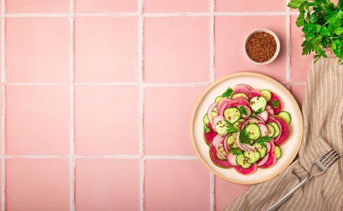 Healthy vegan salad with watermelon radish, cucumber and red onion on pink tile background