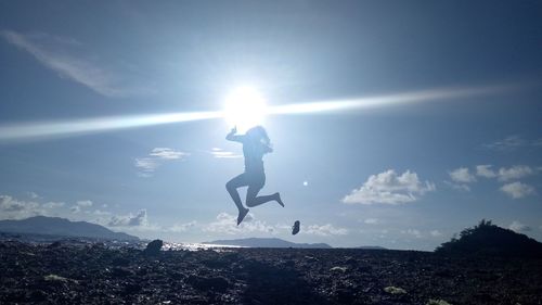 Silhouette young woman jumping on field against sky during sunny day