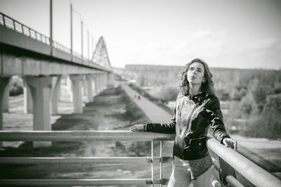 Young woman looking away while standing on bridge against sky