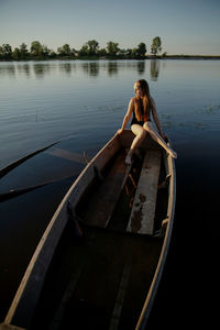 Teenahge girl sitting on boat in lake against sky