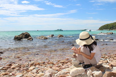 Rear view of woman sitting on rock at beach against sky