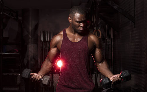 Young man exercising with dumbbells while standing in gym